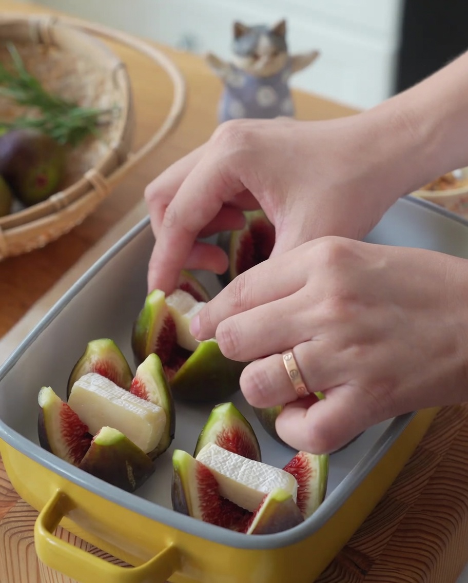 Połówki fig w żółtym naczyniu żaroodpornym wypełniane kawałkami sera Brie.