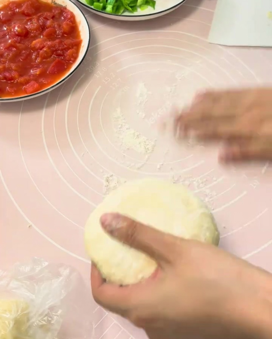 Wyrośnięte ciasto na pizzę wałkowane na różowej silikonowej macie.