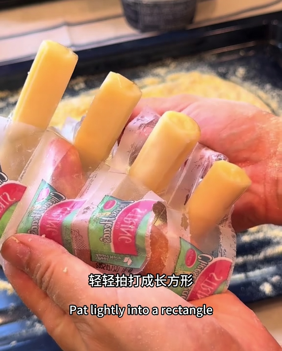 Paluszki z sera mozzarella ułożone wzdłuż krawędzi prostokątnego ciasta na pizzę.
