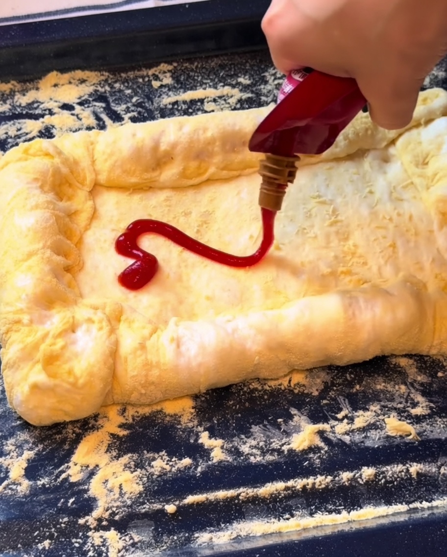 Ketchup rozsmarowywany na spodzie pizzy, a następnie warstwa startego sera mozzarella.