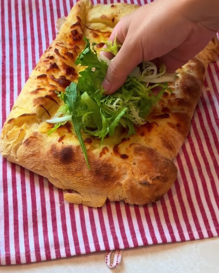 Mieszanka sałat i cienko pokrojona szynka prosciutto układane na wierzchu upieczonej pizzy.