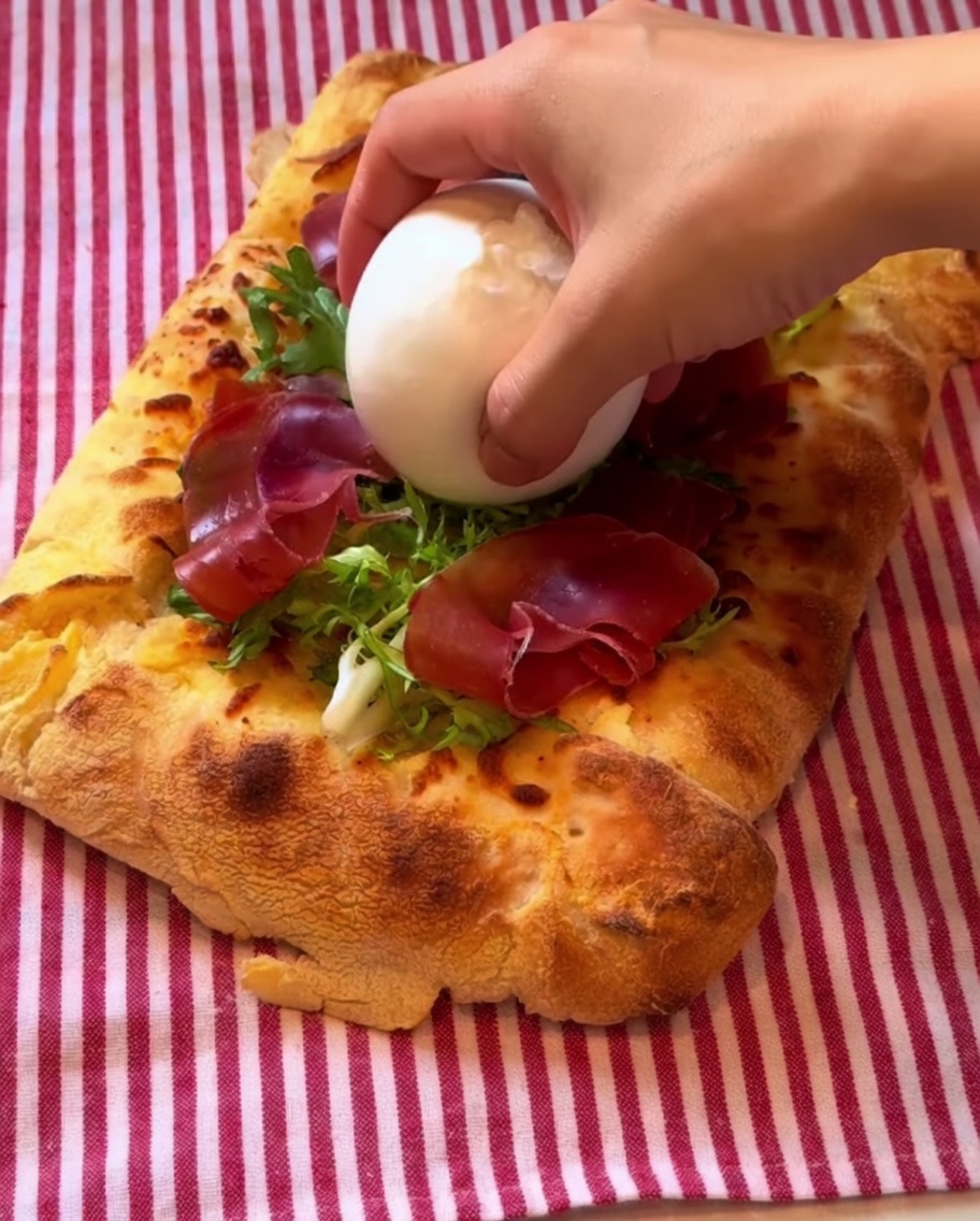 Kulka sera burrata układana na pizzy, skropiona sosem balsamicznym.