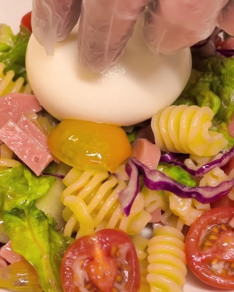 Świeża kulka sera burrata umieszczana w centrum porcji sałatki makaronowej.
