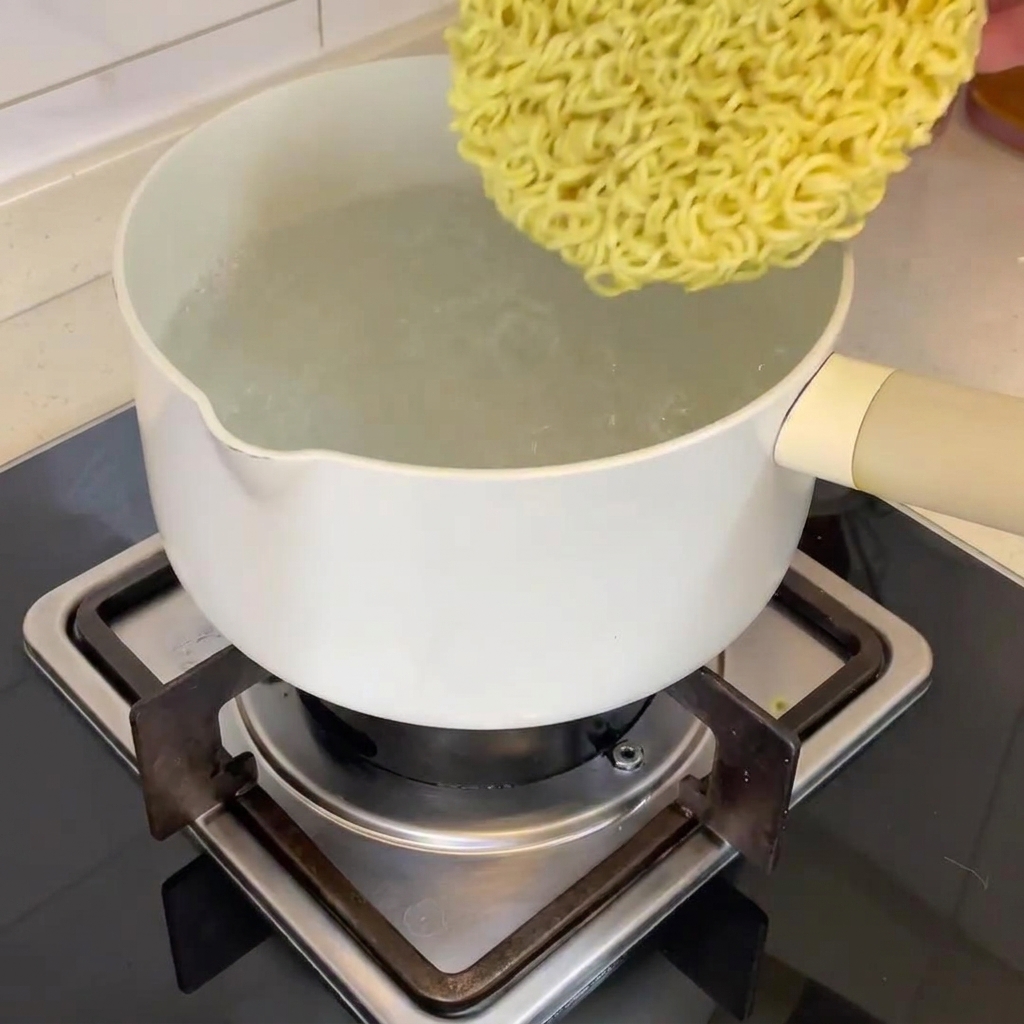 Kawałek suszonego makaronu ramen wkładany do garnka z wrzątkiem.