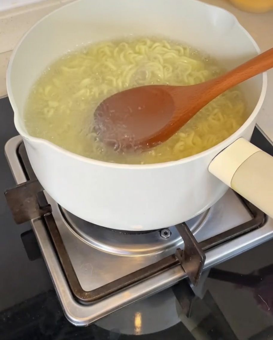 Chochla wlewa wrzącą wodę z makaronu do miski z bazą.