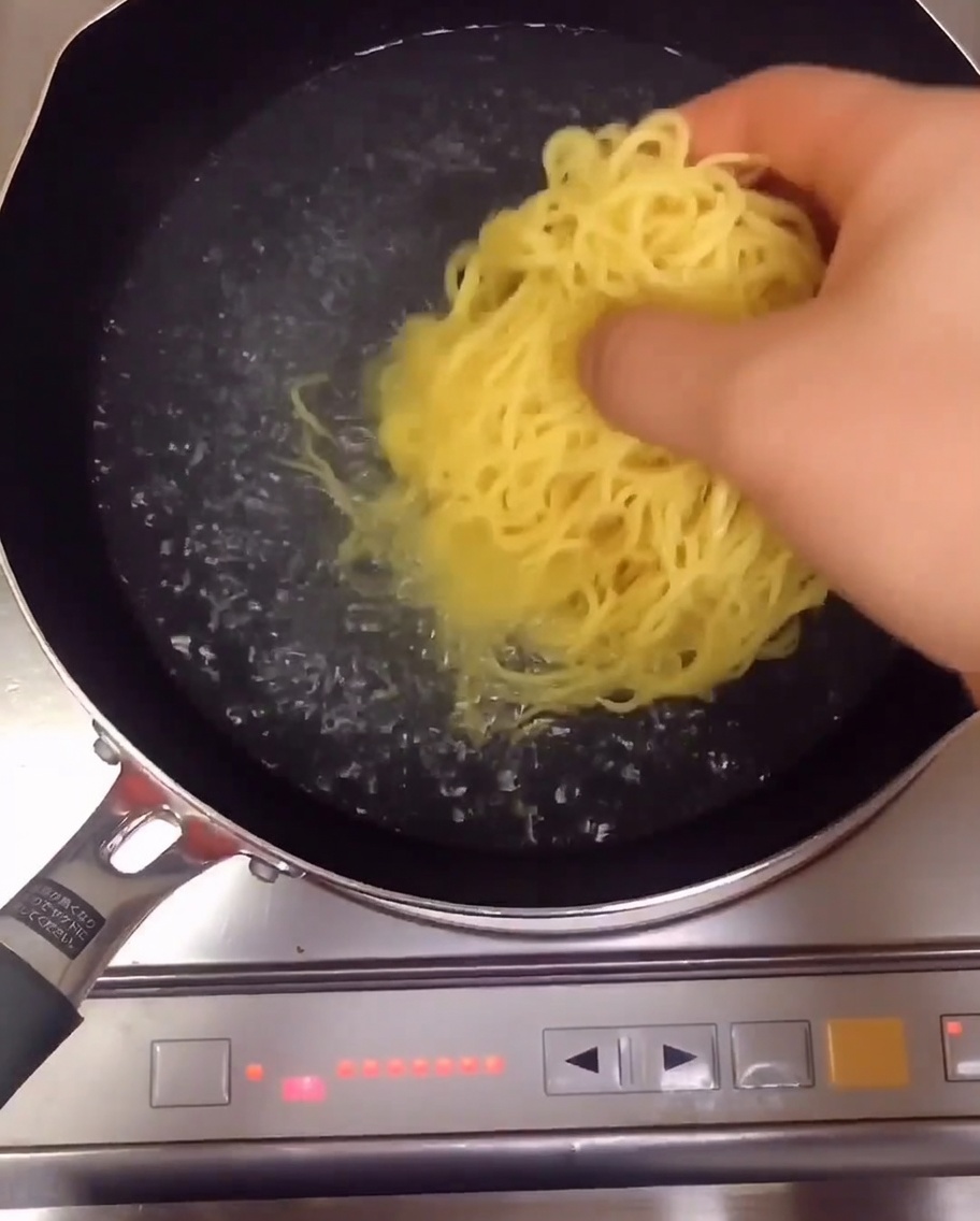 Żółty makaron ramen gotujący się w garnku z wodą na kuchence.