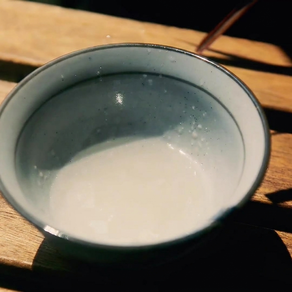 Mała ceramiczna miseczka na drewnianej powierzchni zawierająca mieszankę sake, cukru i sosu sojowego.