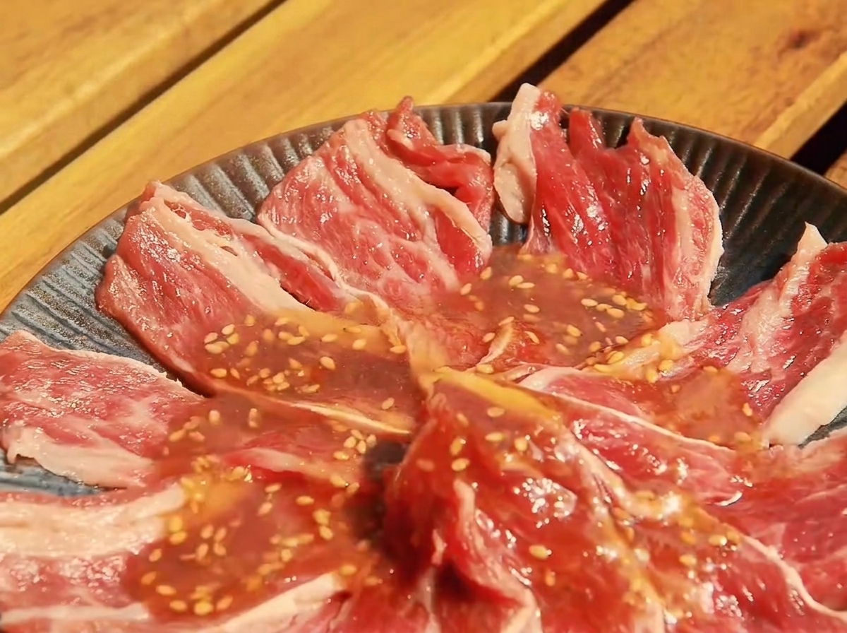 Cienkie plastry surowej wołowiny w płaskim naczyniu, pokryte przygotowanym sosem Yakiniku.