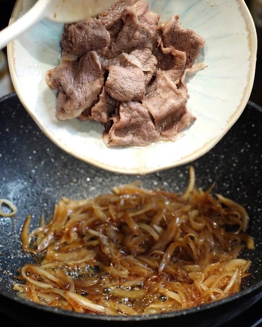 Ciemny sos teriyaki wlewany na patelnię z mięsem i cebulą.