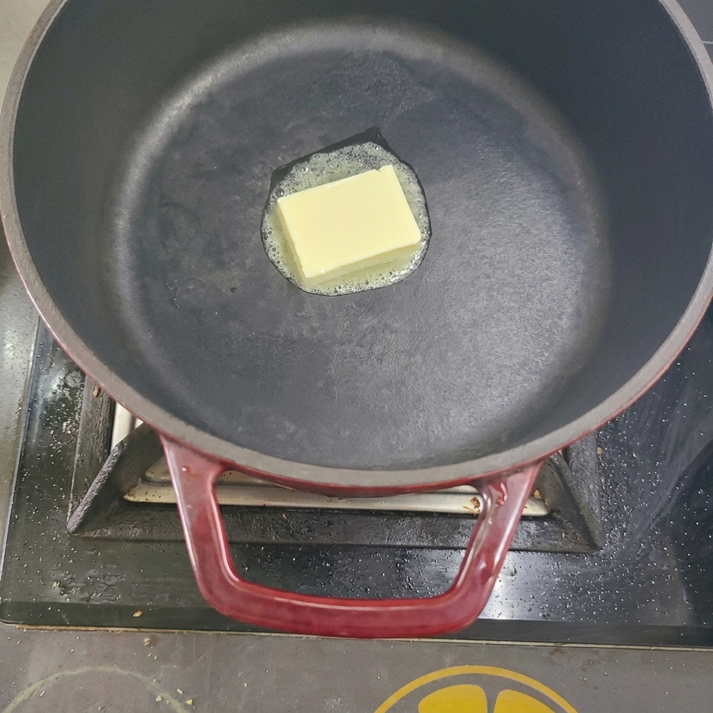 Kostka masła topniejąca w czarnym garnku na kuchence.