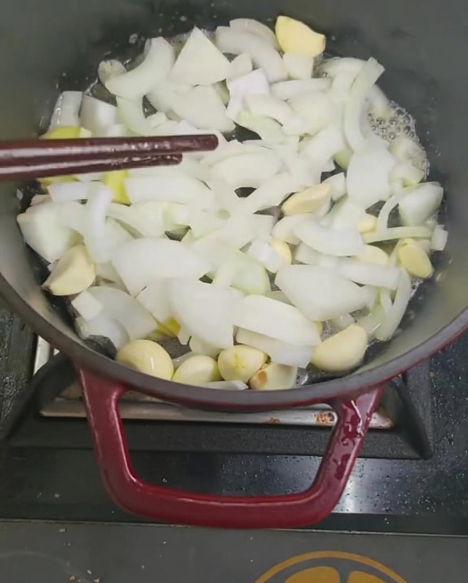 Podsmażanie cebuli i czosnku w garnku za pomocą pałeczek.