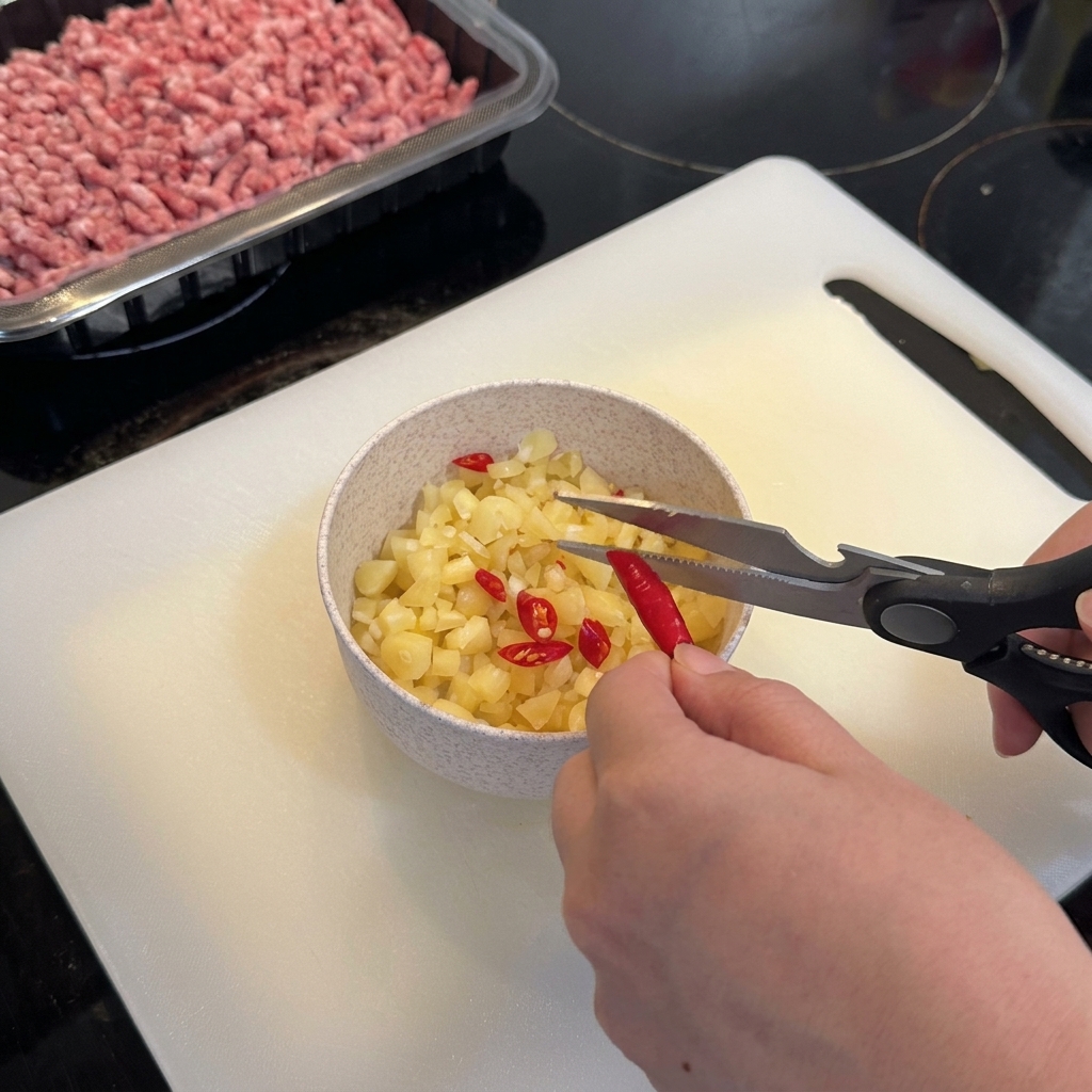 Nożyce kuchenne tnące czerwone papryczki chili birds eye prosto do miski z czosnkiem.