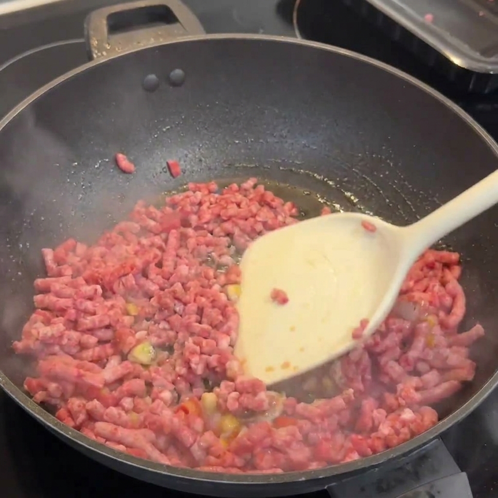 Mielona wołowina Wagyu brązowiejąca w woku, rozbijana białą łopatką.