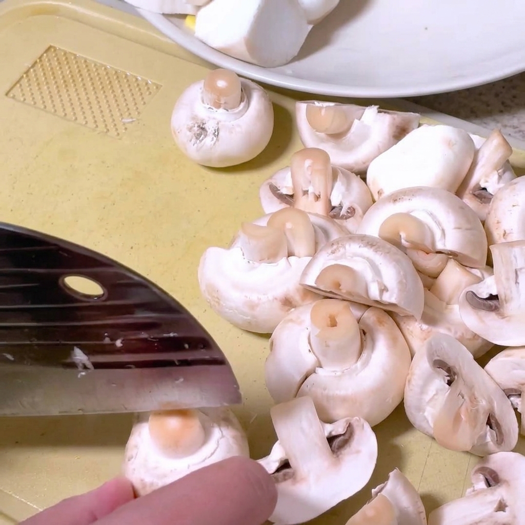 Pieczarki przekrawane na pół nożem kuchennym na desce do krojenia.