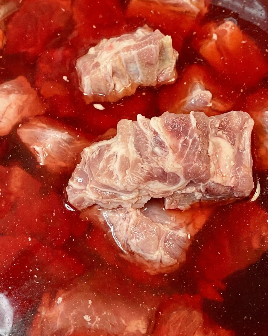 Surowe kości wieprzowe zanurzone w misce z czerwoną, krwistą wodą.
