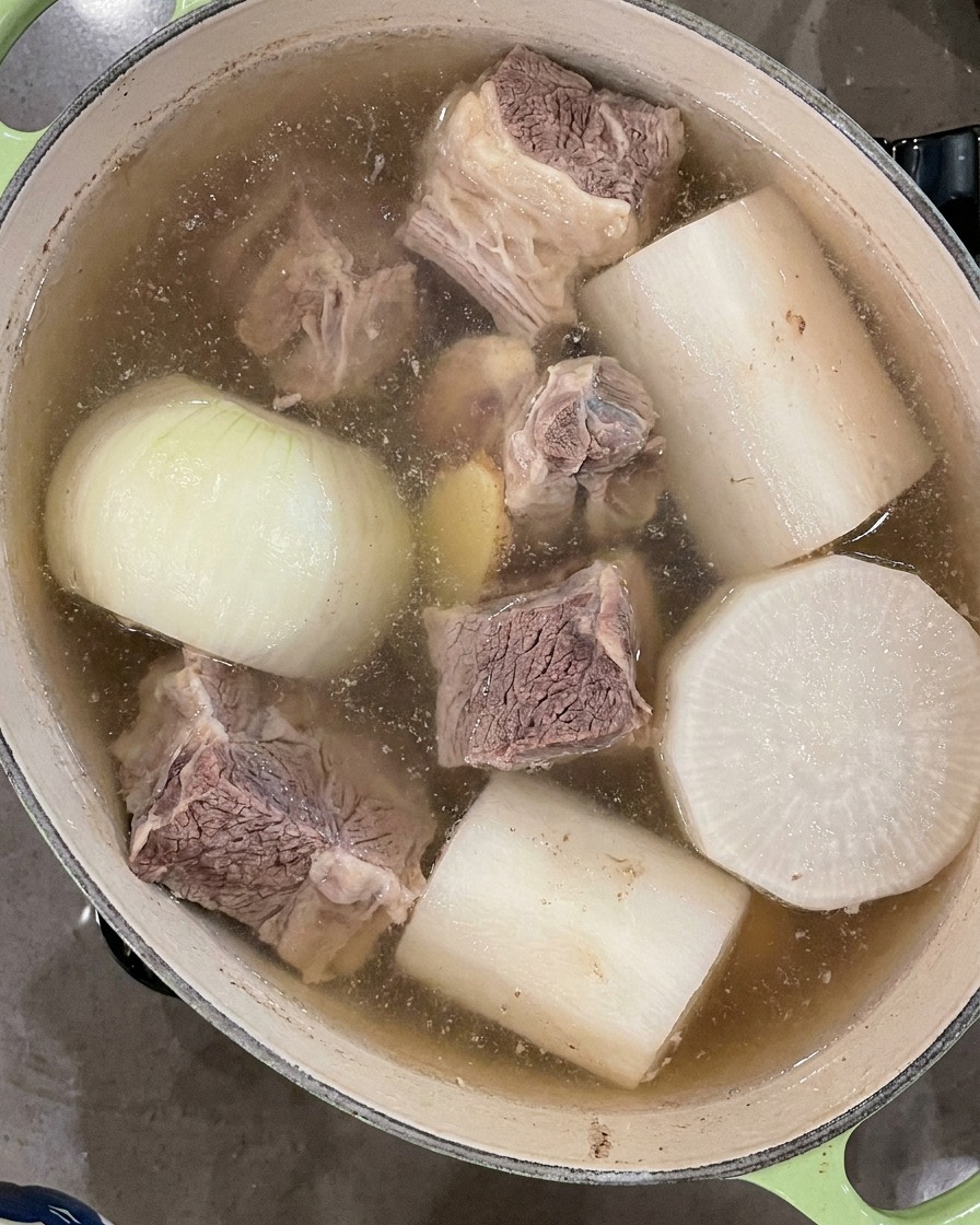 Czarna łyżka wazowa zbierająca pianę z powierzchni gotującej się zupy.