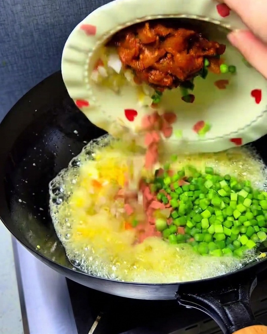 Posiekane kimchi, szynka, kurczak i pędy czosnku wrzucane z talerza do woka z jajkami.