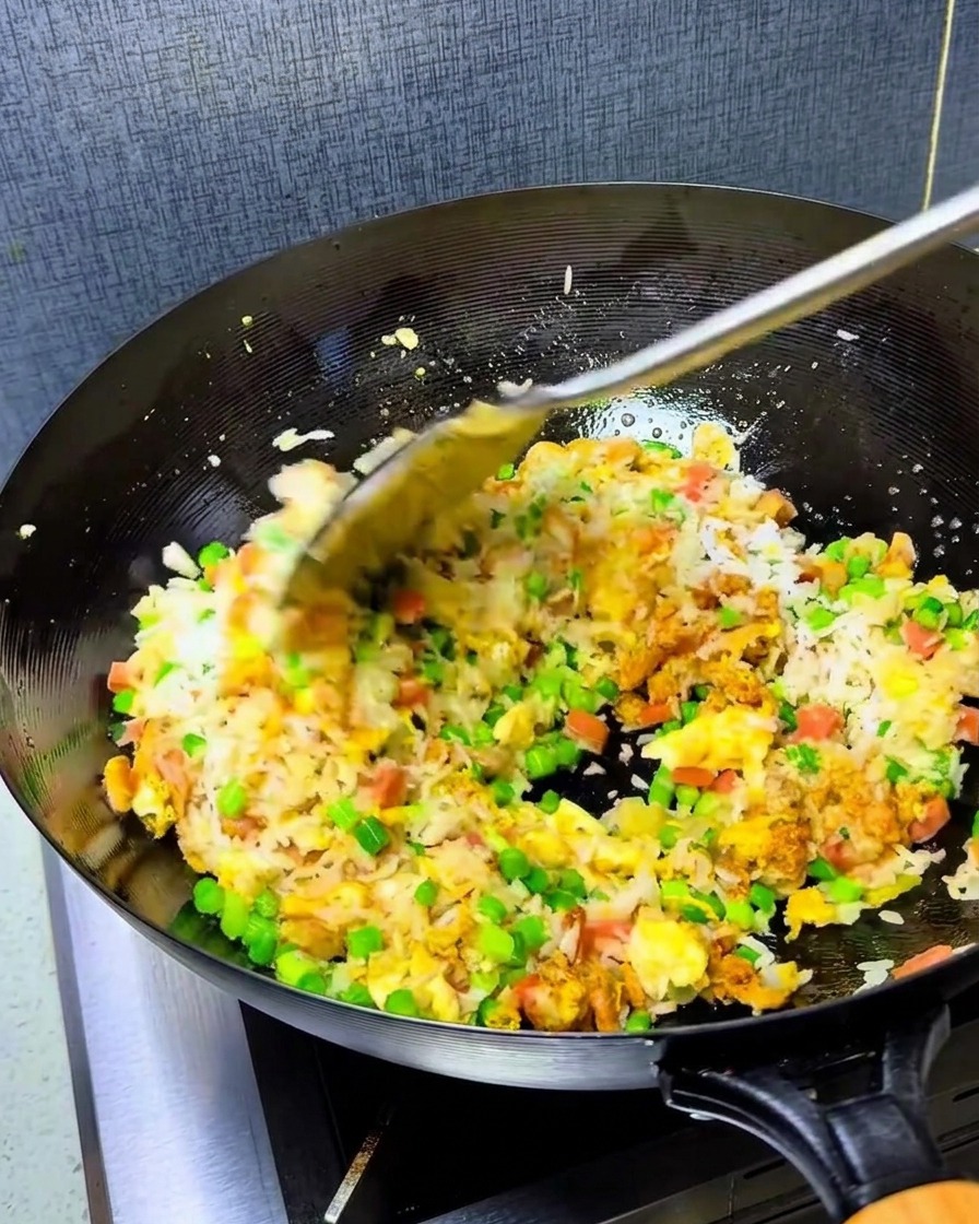 Łyżka wibrującego czerwonego oleju chili dodawana do ryżu w gorącym woku.