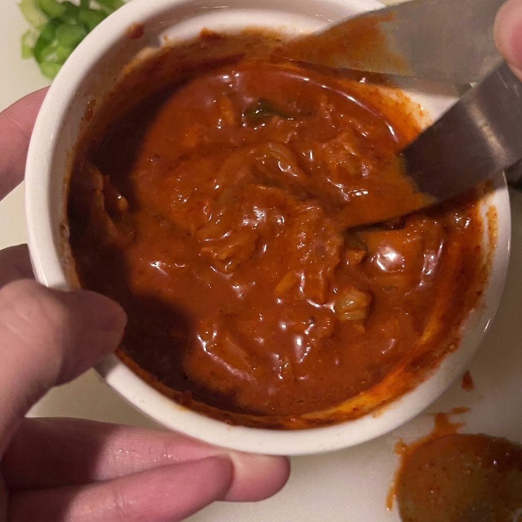 Para nożyczek kuchennych tnie kawałki kimchi bezpośrednio w misce z sosem.