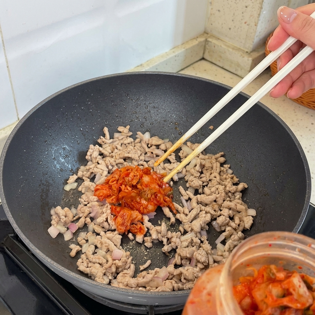 Kawałki kimchi dodawane do mieszanki mięsa i szalotki na patelni.