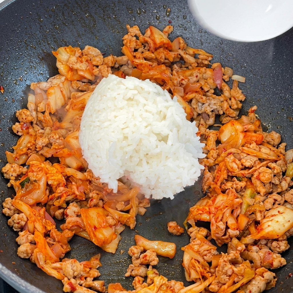 Ugotowany ryż dodawany do patelni z mięsem i kimchi.