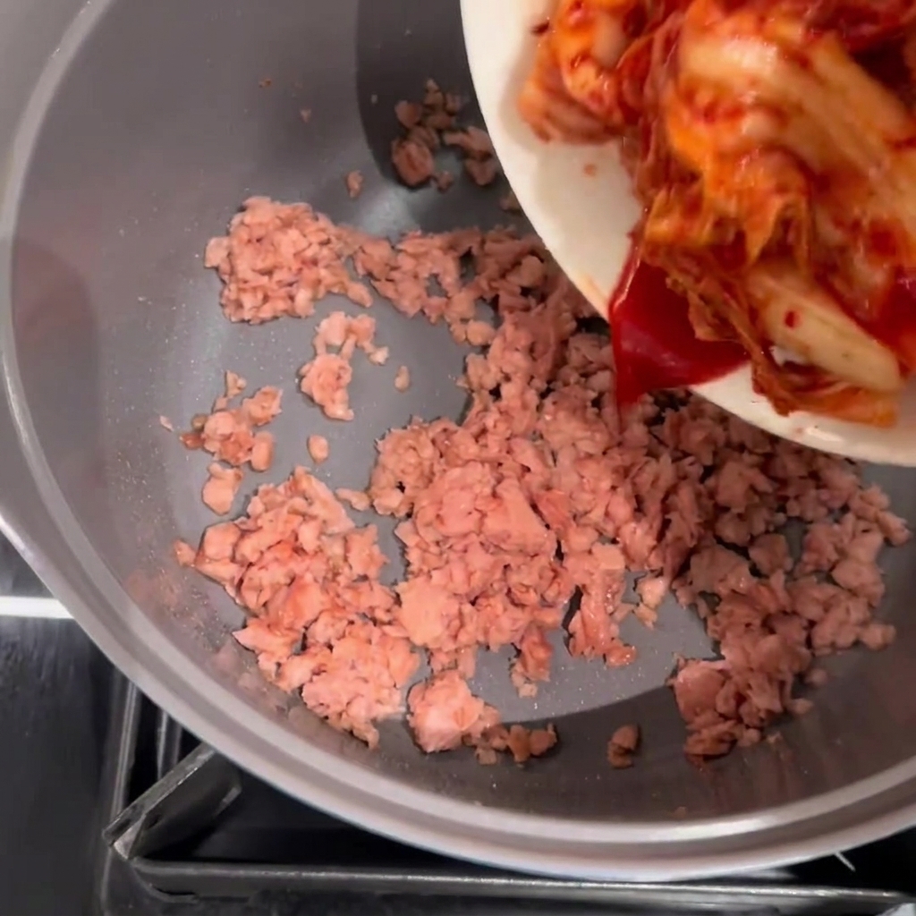 Kimchi dodawane do garnka z podsmażonym Spamem.