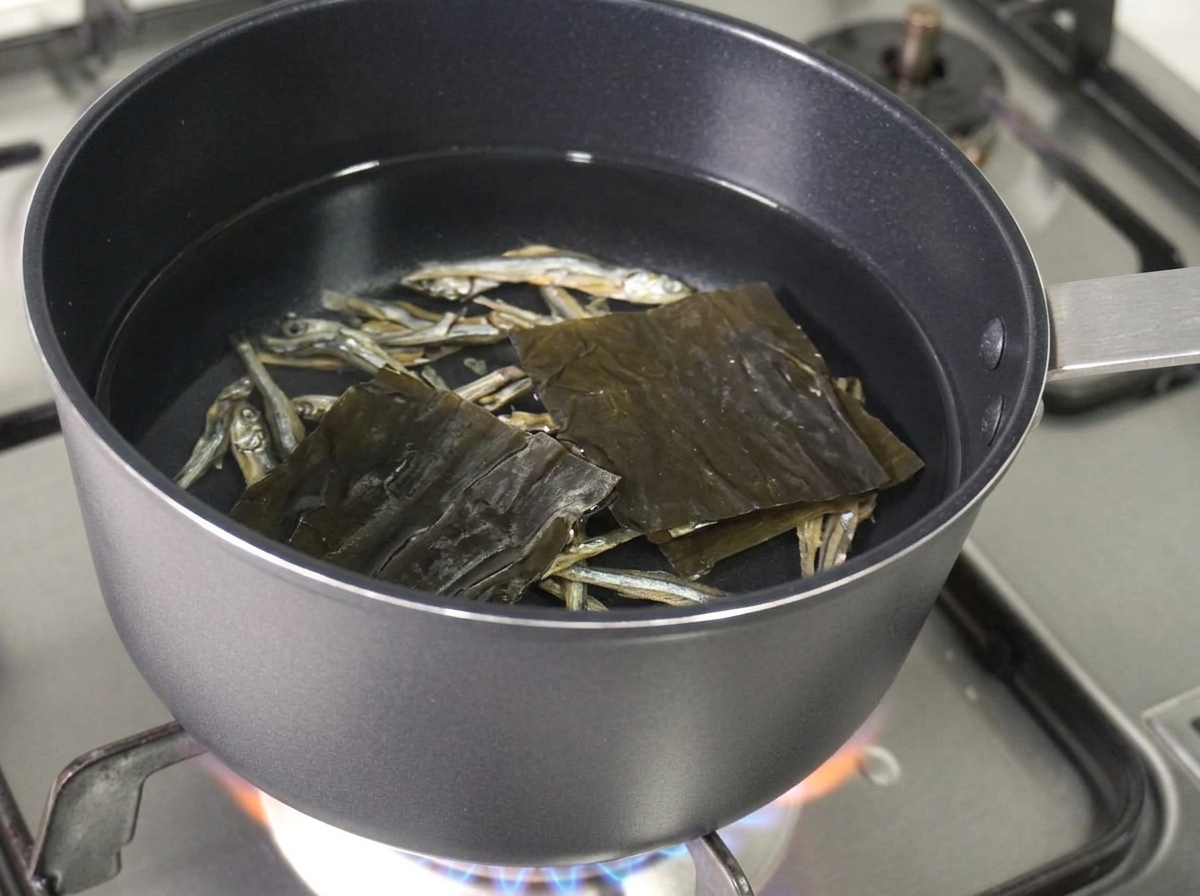 Suszone anchois i kwadratowy kawałek suszonego kelpu pływające w garnku z wodą.