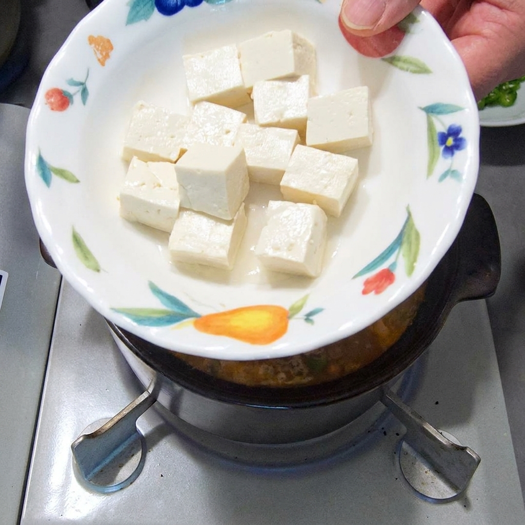 Miękkie, białe kostki tofu wrzucane do gotującego się gulaszu.