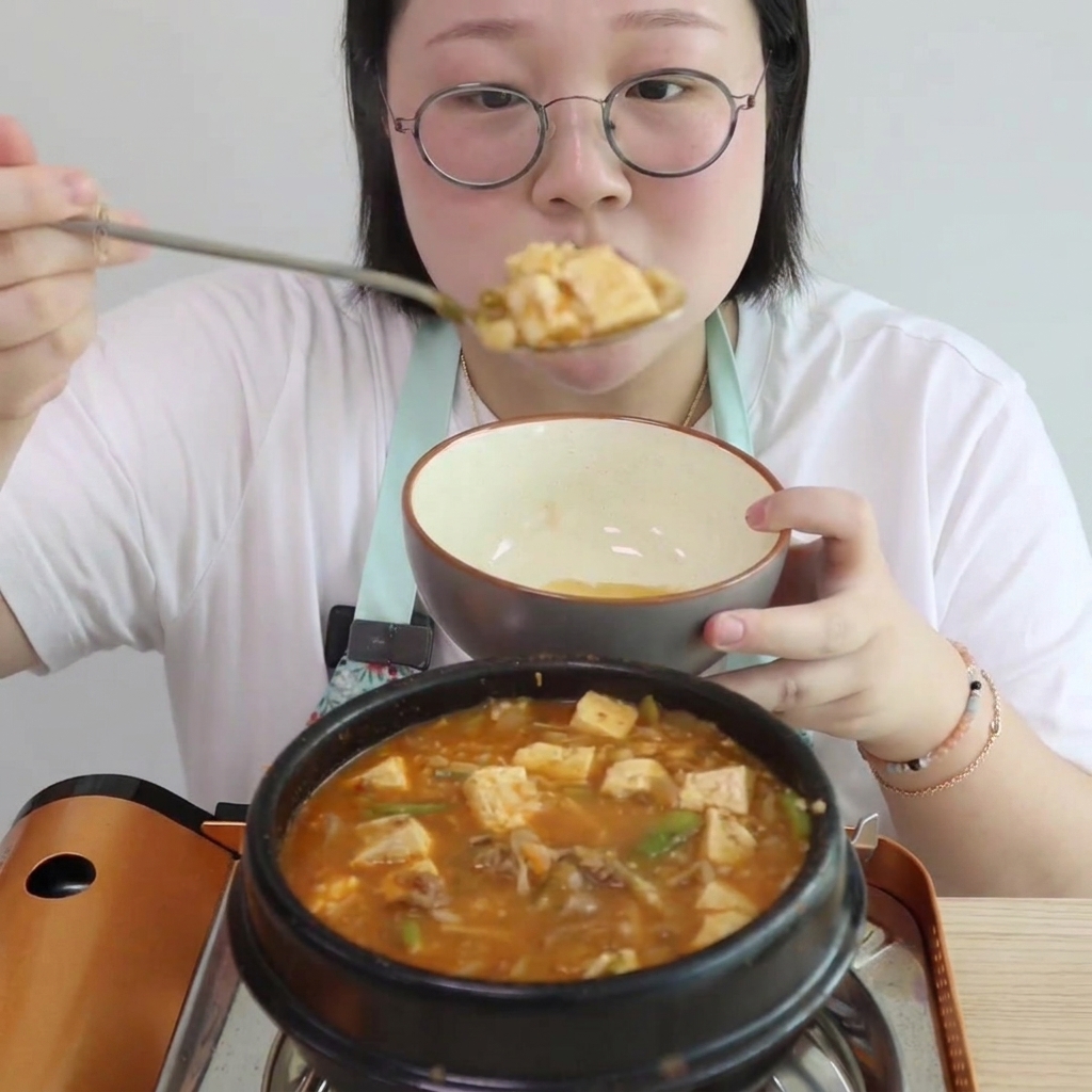 Pokrojone w kostkę tofu i małe porcje grzybów enoki dodawane do bulgoczącej zupy.