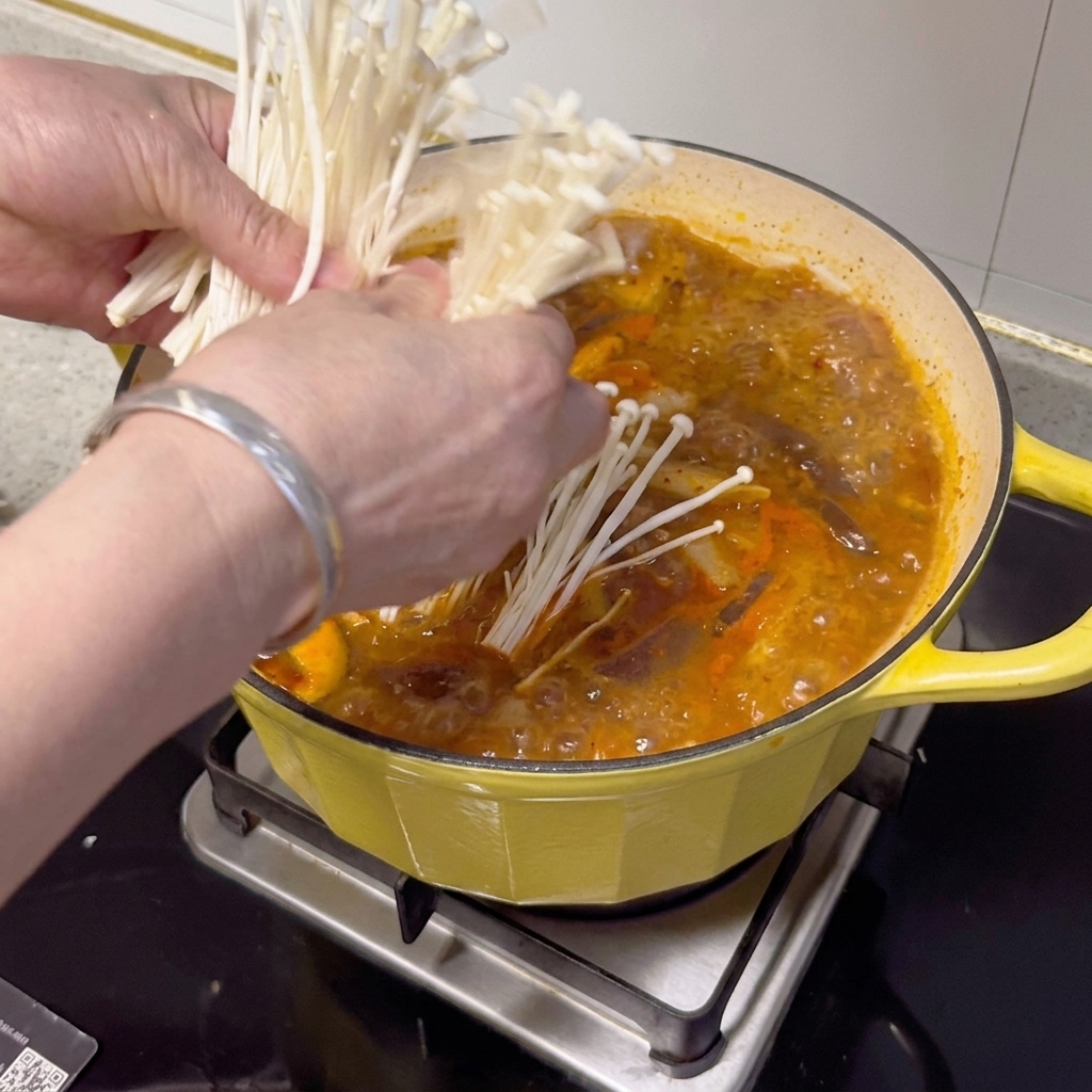 Grzyby enoki, zielona cebulka i plasterki chili ułożone na wierzchu gotowego gulaszu.