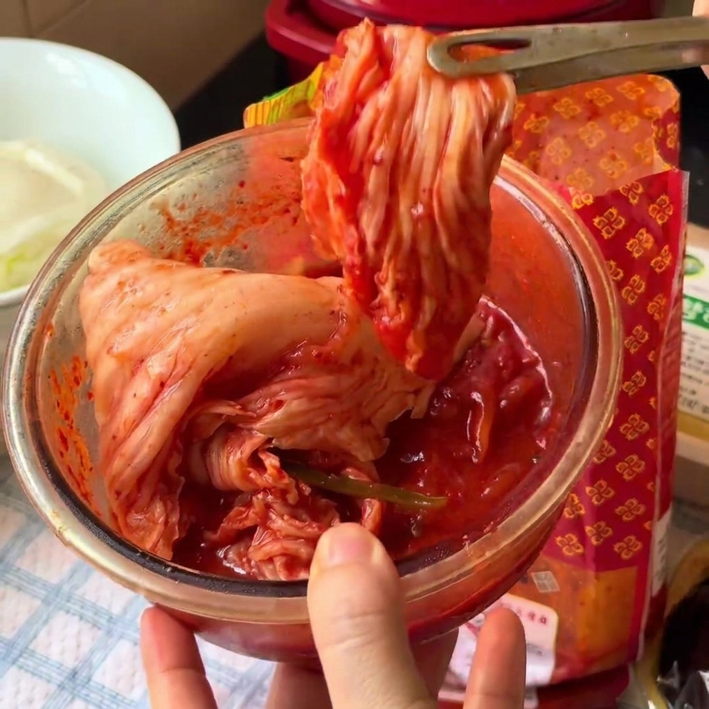 Kimchi krojone na mniejsze kawałki wewnątrz szklanej miski przy użyciu nożyczek kuchennych.