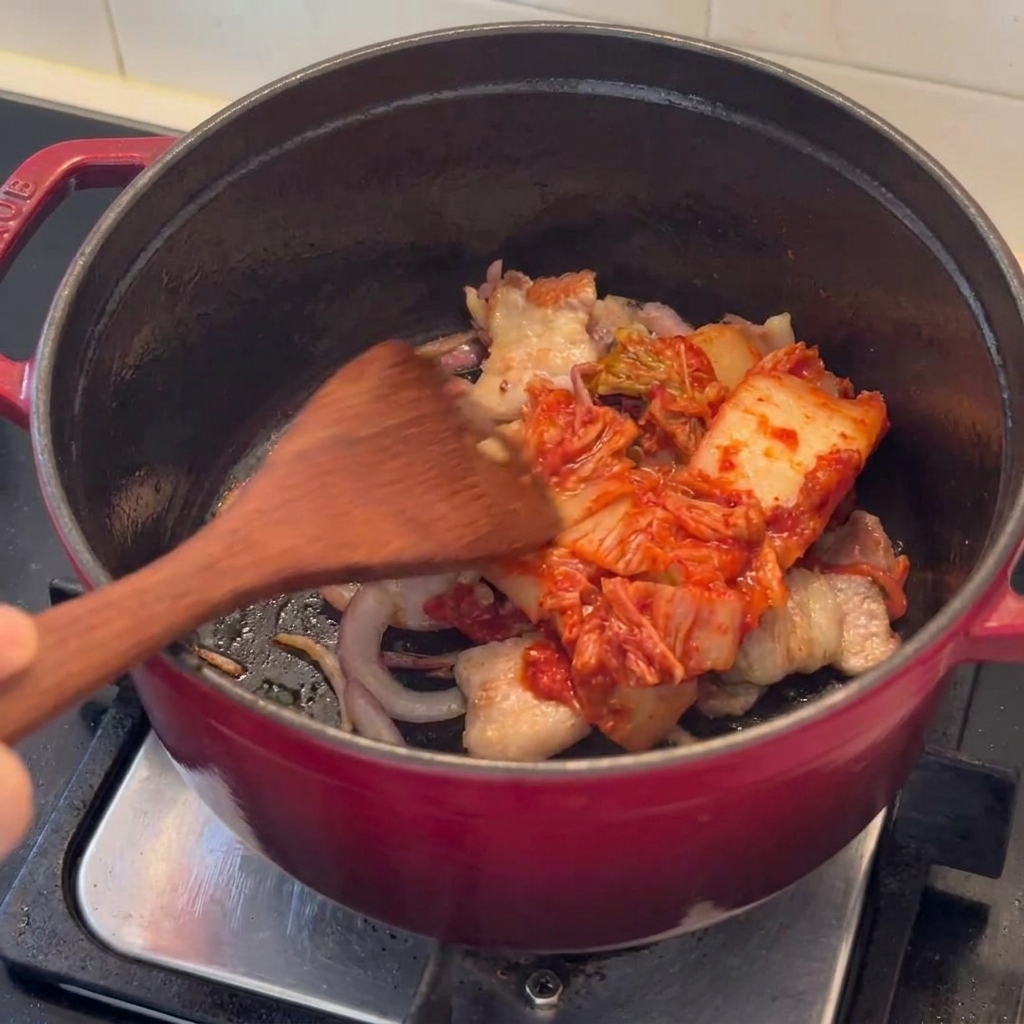 Kawałki kimchi podsmażane w garnku z rumianym boczkiem wieprzowym.