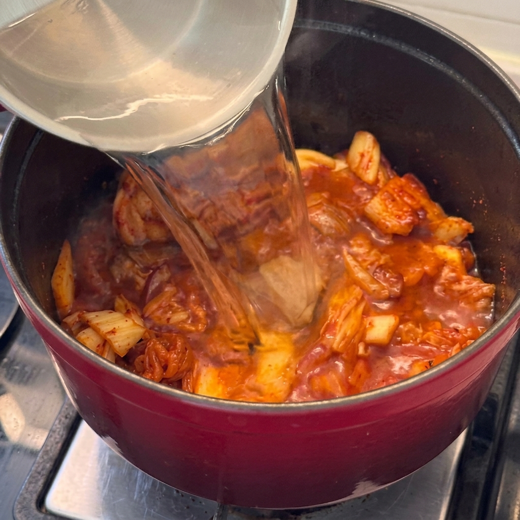Woda wlewana do garnka z mięsem i kimchi, by stworzyć płynną bazę zupy.