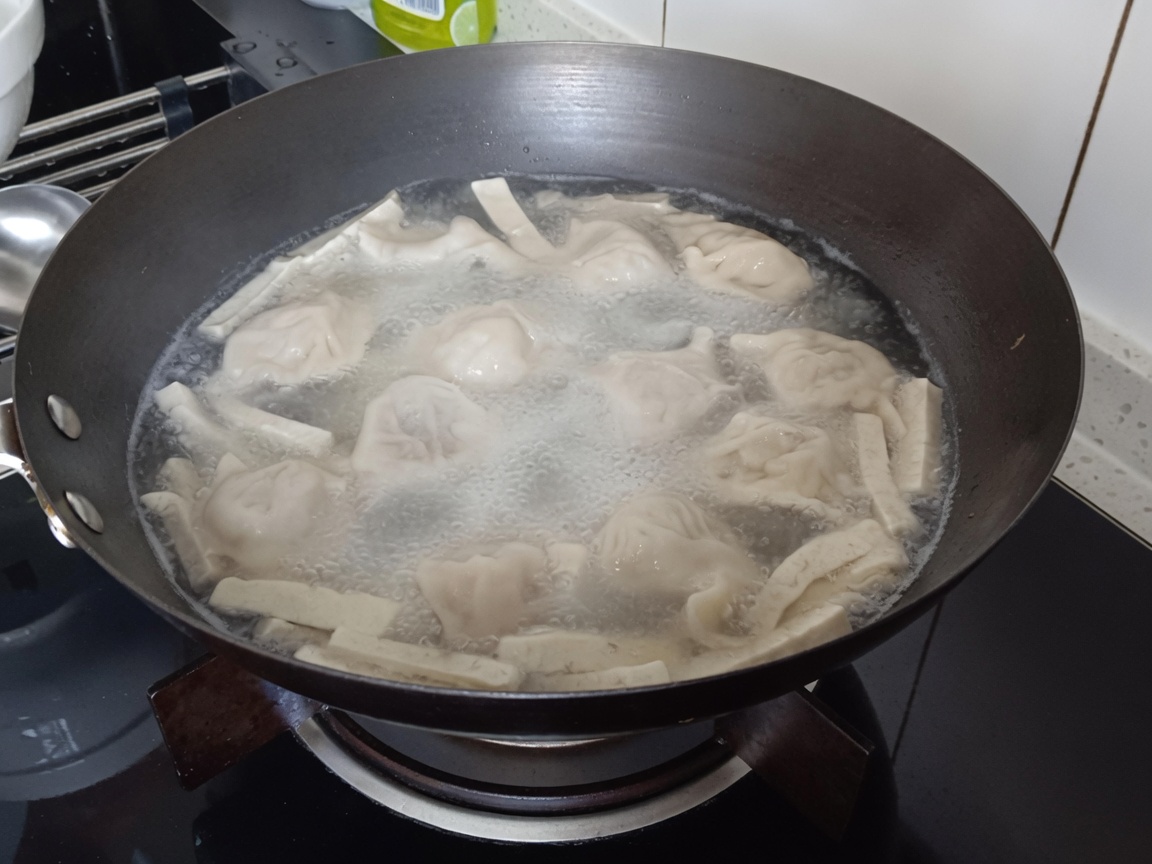 Zbliżenie na makaron vermicelli zanurzany w garnku z pierożkami i tofu.