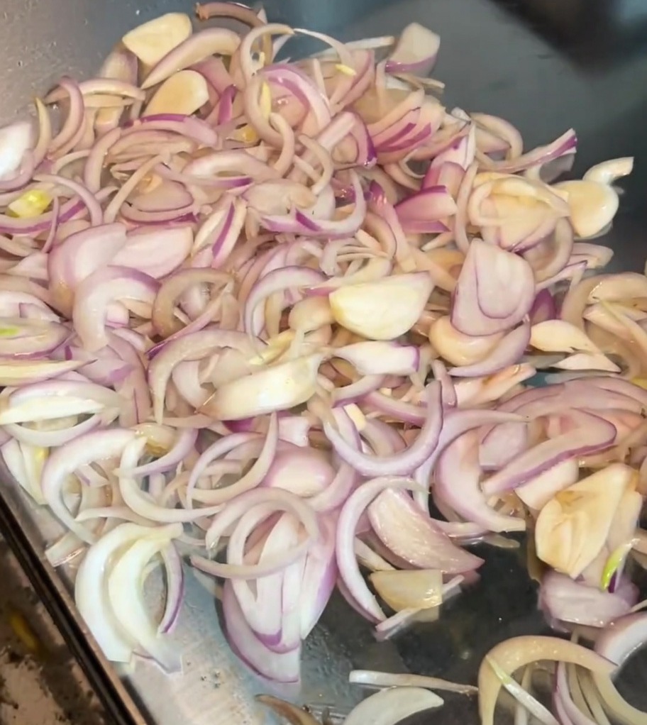 Pokrojona cebula mieszana na gorącym grillu metalową łopatką.