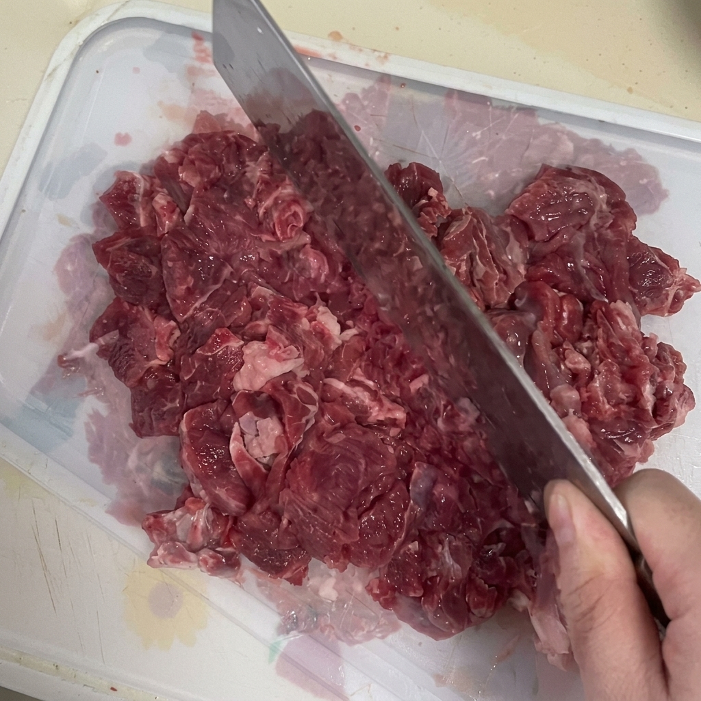 Mięso wołowe drobno siekane tasakiem na desce do krojenia.