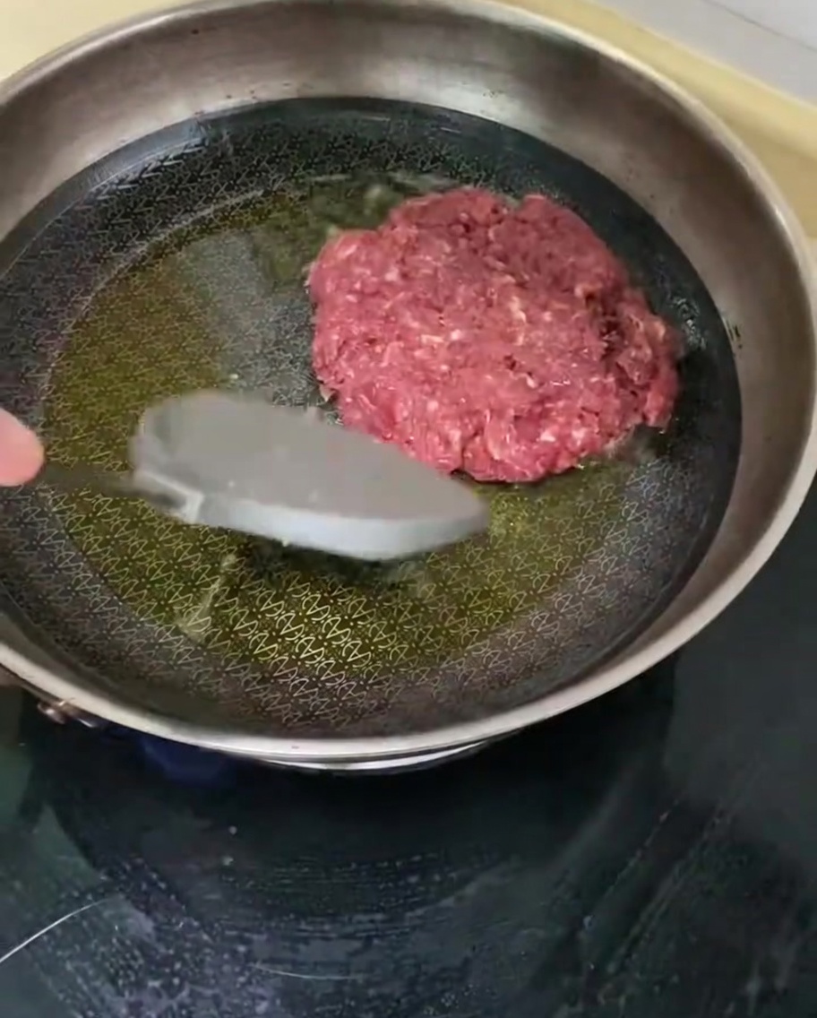 Kotlet wołowy smażący się na gorącej patelni z oliwą.