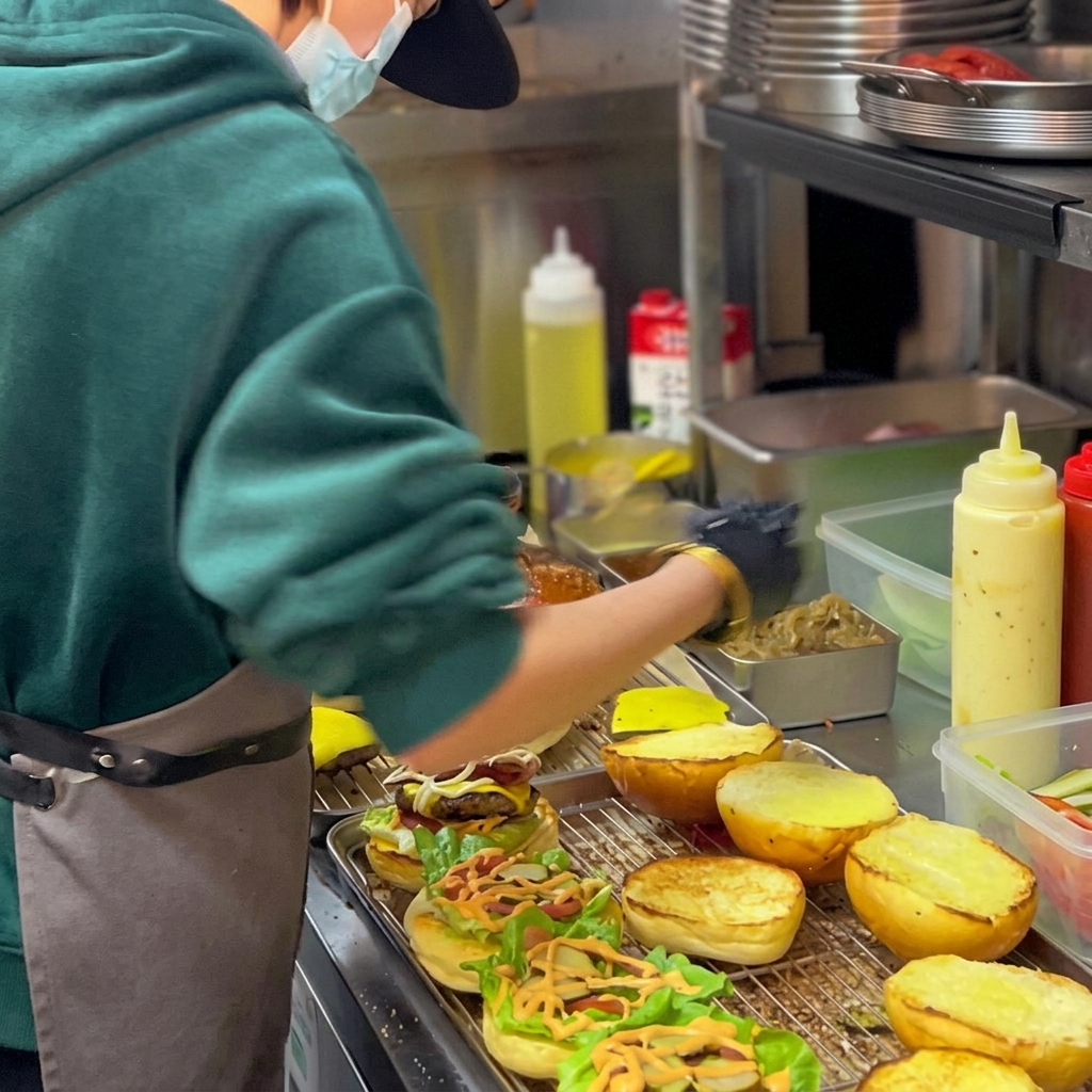 Świeżo złożony burger z soczystym kotletem wołowym, roztopionym serem, chrupiącą sałatą, pomidorem i cebulą karmelizowaną w czerwonym winie, podany w opieczonej bułce.