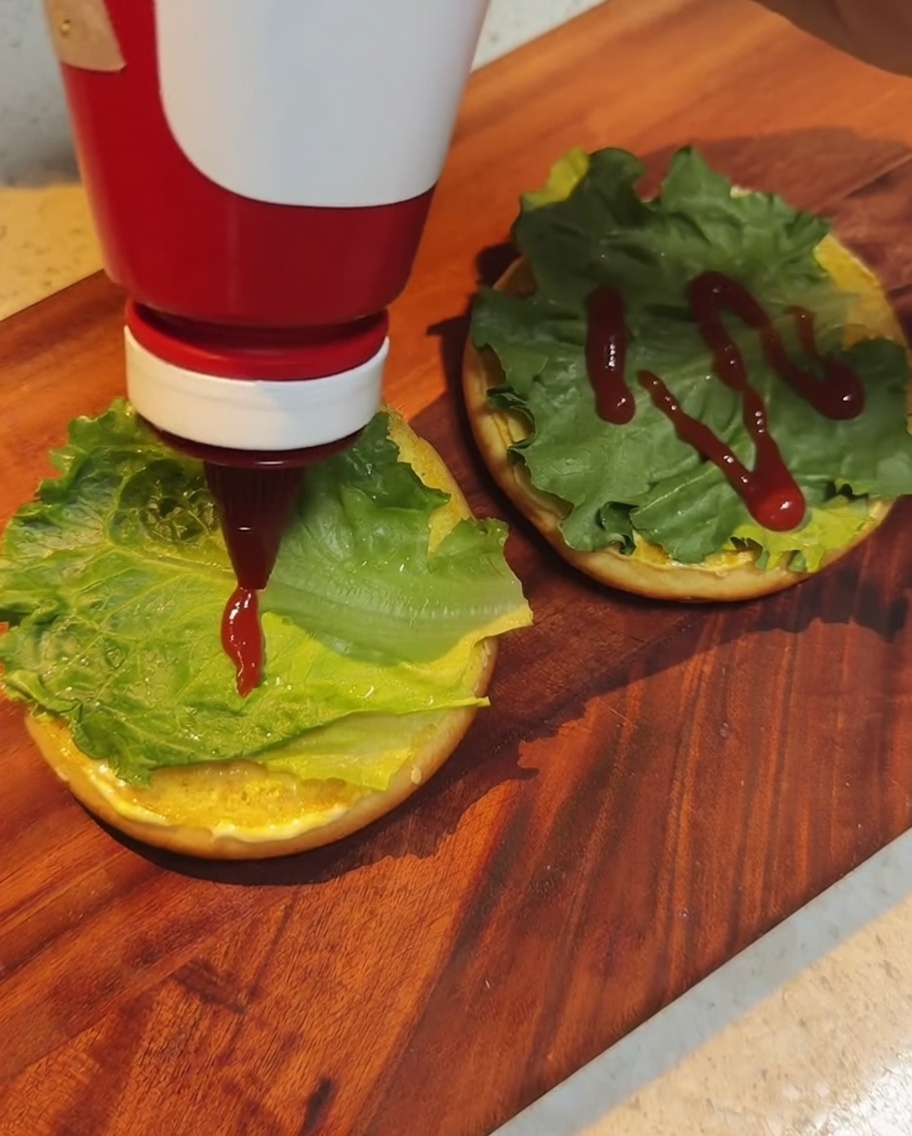 Czerwony ketchup skrapiany na liście sałaty umieszczone na bułce.
