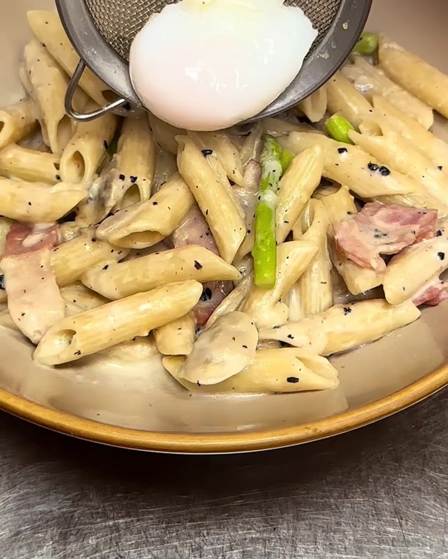Kremowy makaron penne nałożony do miski, starannie zwieńczony ugotowanym jajkiem w koszulce.