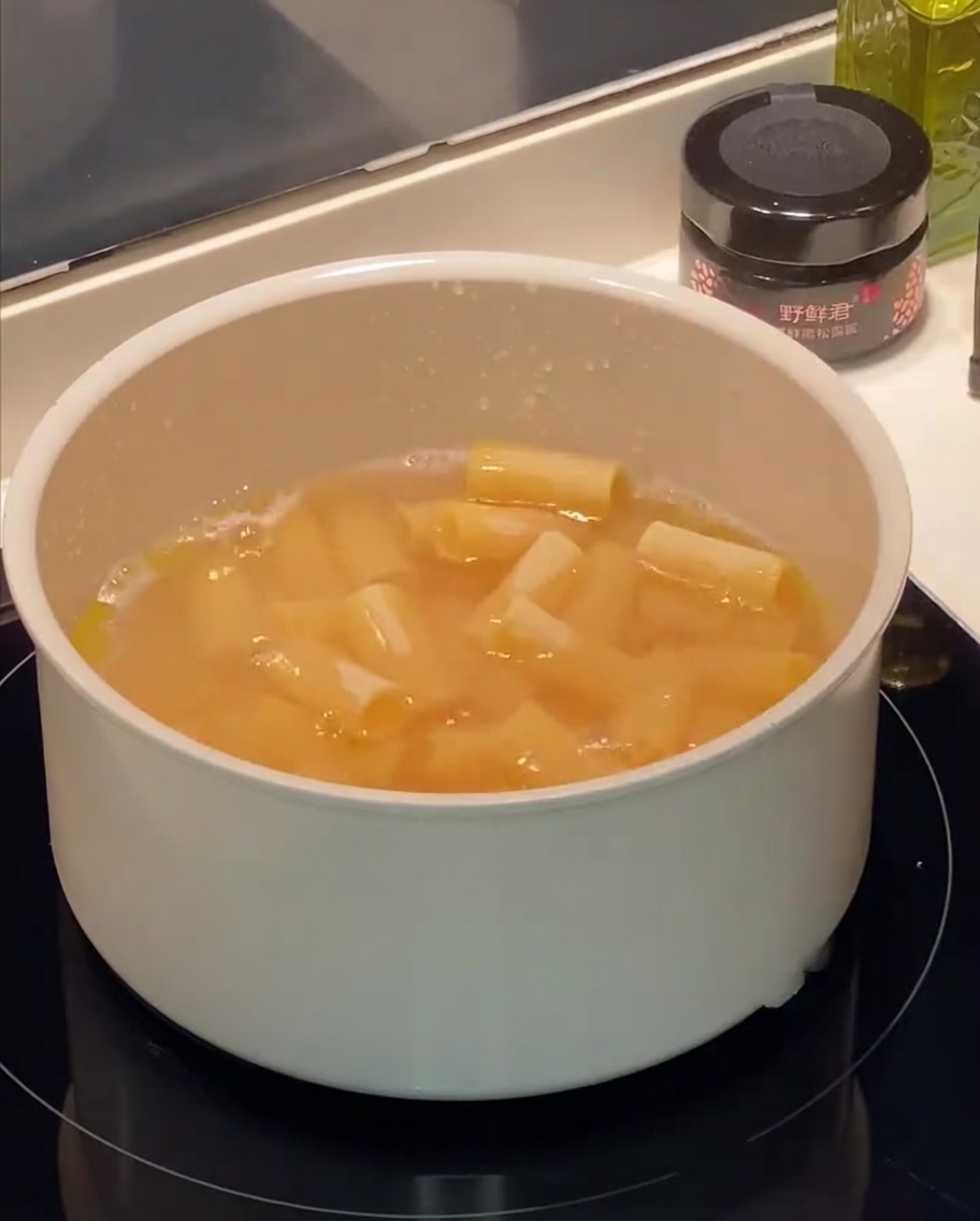 Makaron rigatoni gotujący się w garnku z widocznymi bąbelkami i kroplami oliwy na powierzchni.