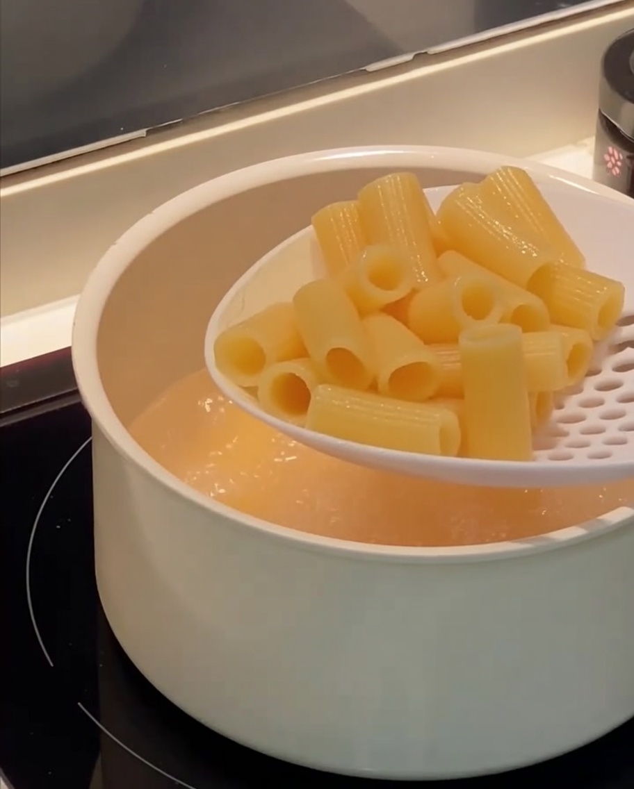 Łyżka cedzakowa wyjmująca ugotowane rigatoni z wrzącej wody.
