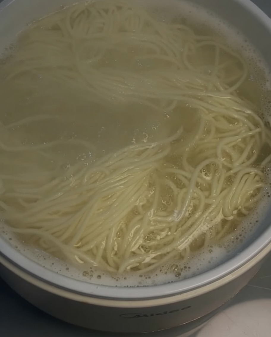 Łyżka cedzakowa wyciągająca ugotowany makaron z garnka.