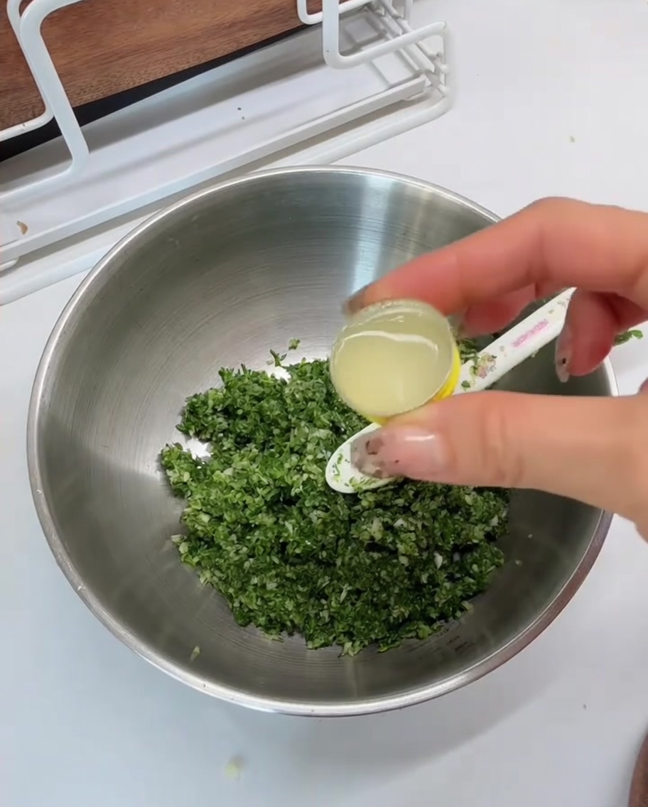 Sok z cytryny wlewany z łyżeczki do metalowej miski z zieloną mieszanką.