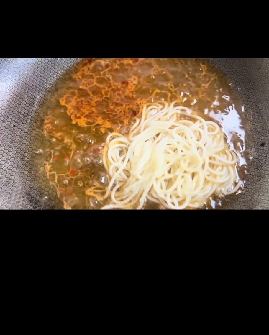 Ugotowane spaghetti przekładane bezpośrednio do woka, by wymieszać z sosem.