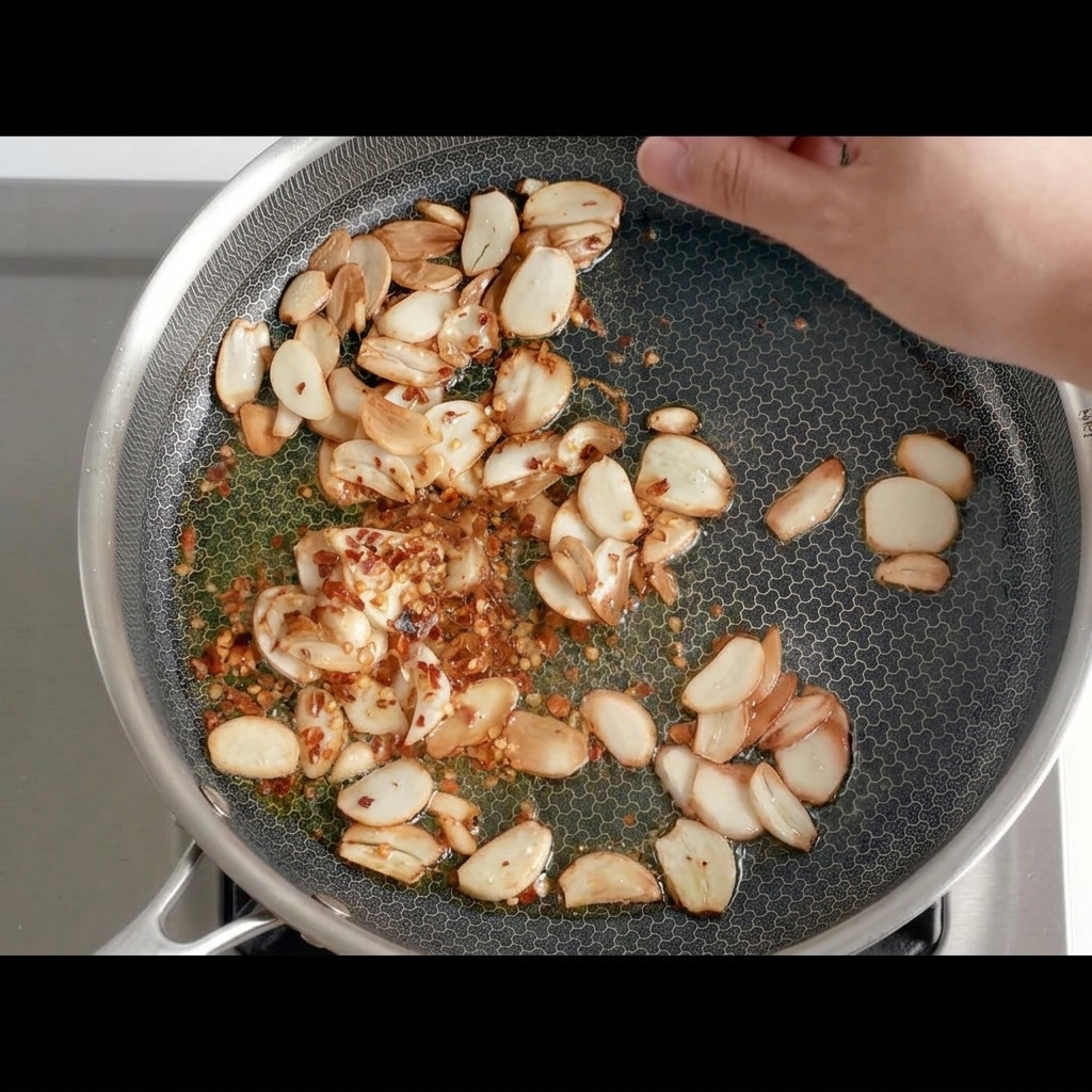 Kawałki suszonego chili dodawane do patelni ze złocistym czosnkiem.