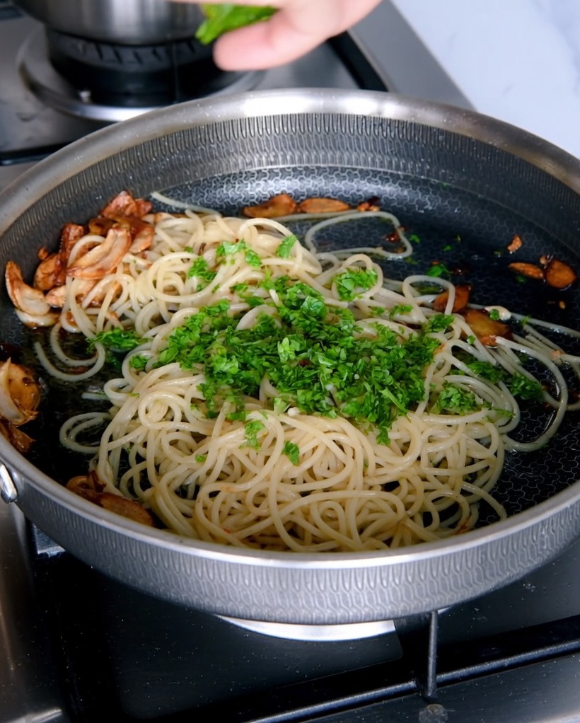 Posiekana świeża natka pietruszki dodawana do patelni ze spaghetti.