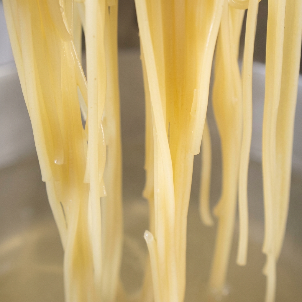 Ugotowany makaron spaghetti dodawany na patelnię z przyprawioną oliwą z czosnkiem i chili.