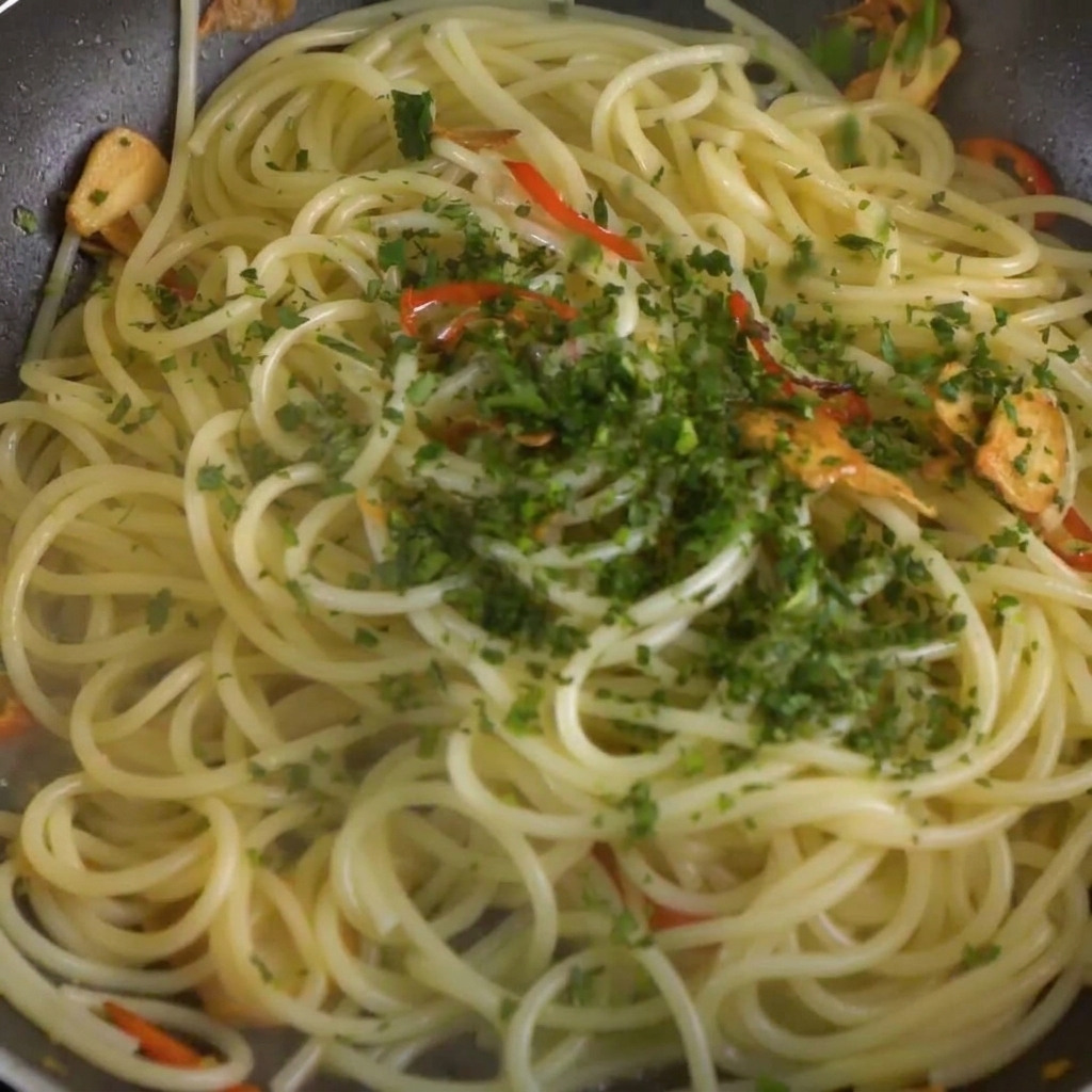 Posiekana świeża natka pietruszki rozsypywana nad spaghetti z mieszanką chili i czosnku na patelni.