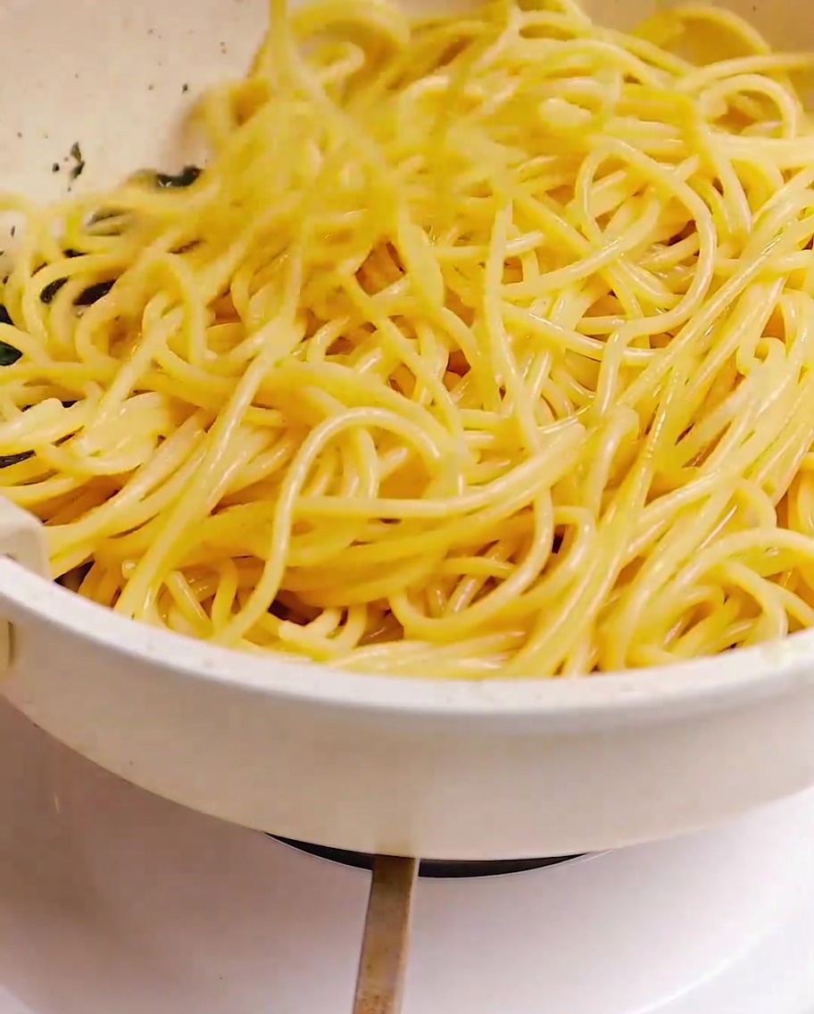 Ugotowane spaghetti mieszane na patelni z boczkiem, czosnkiem i ziołami.